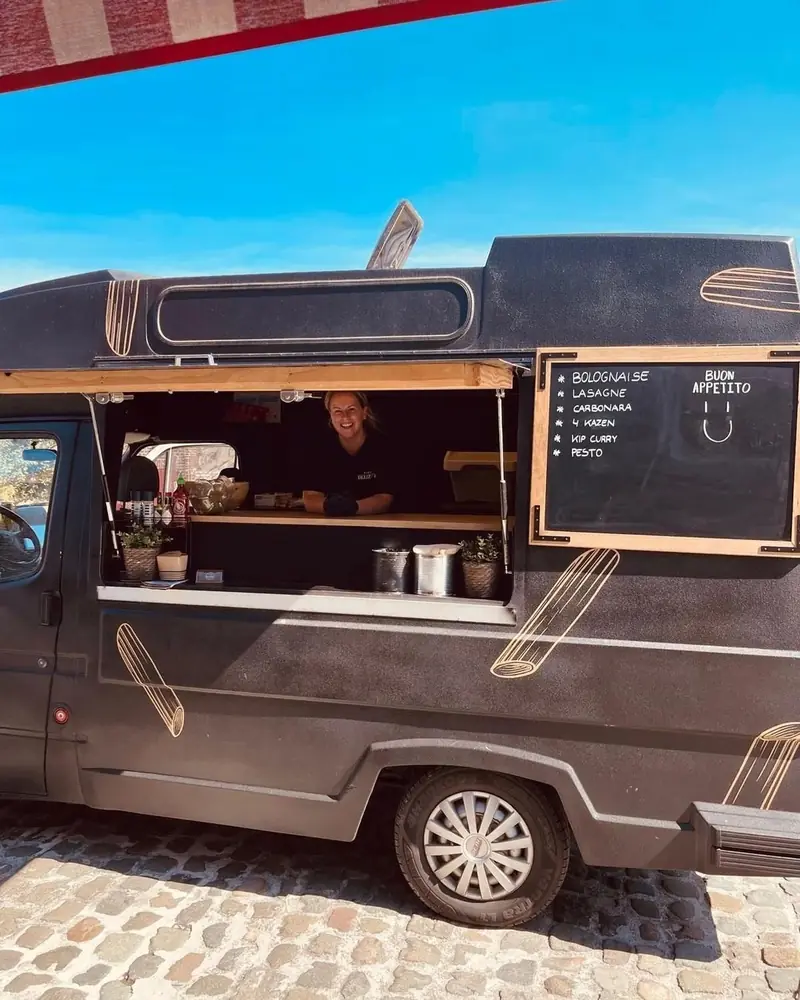 Zwarte oldtimer-foodtruck van Pasta Deliziosa op kasseien, met open luifel en krijtbord