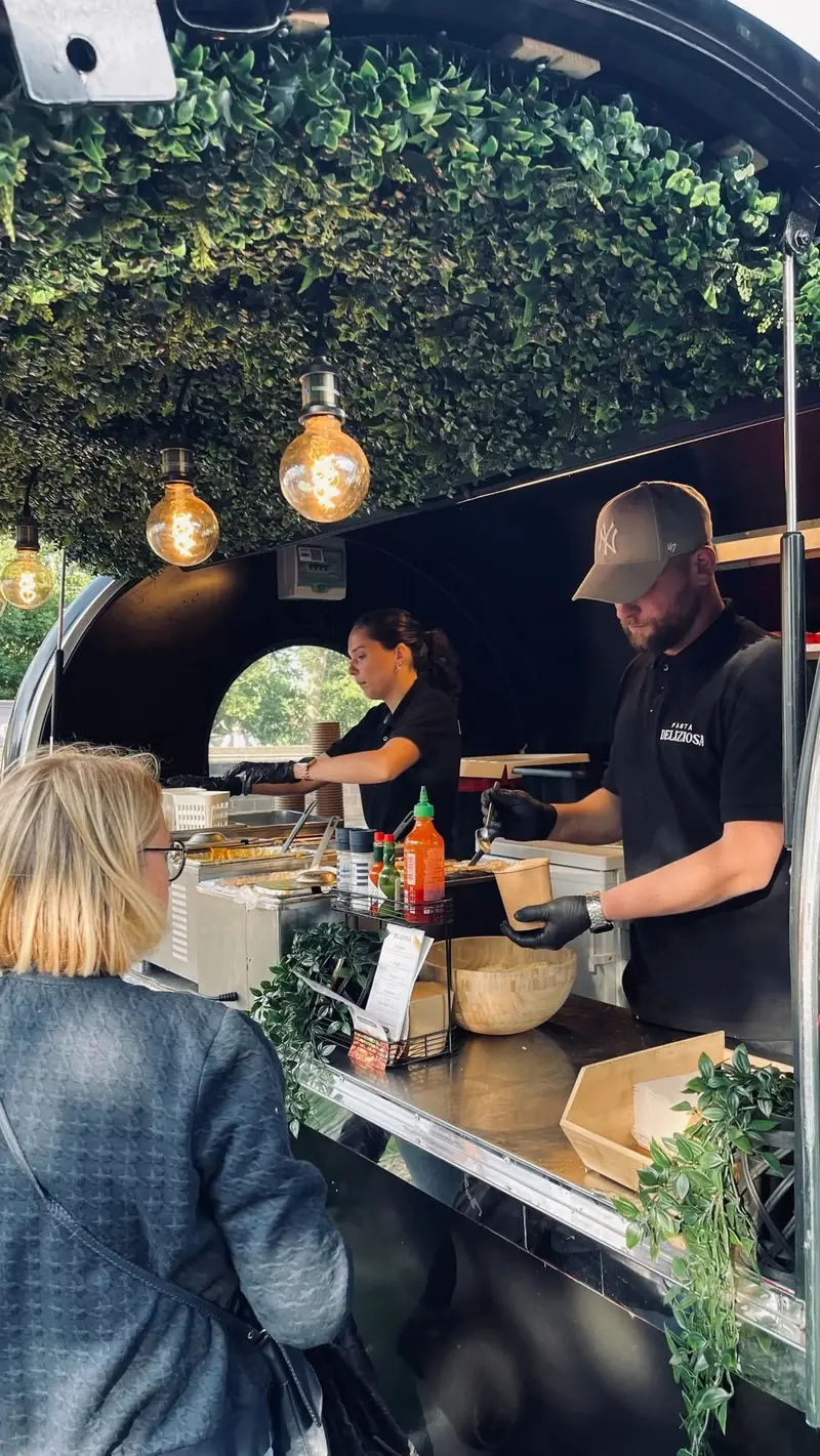 Een gaste krijgt haar pasta aan de toog van de foodtrailer