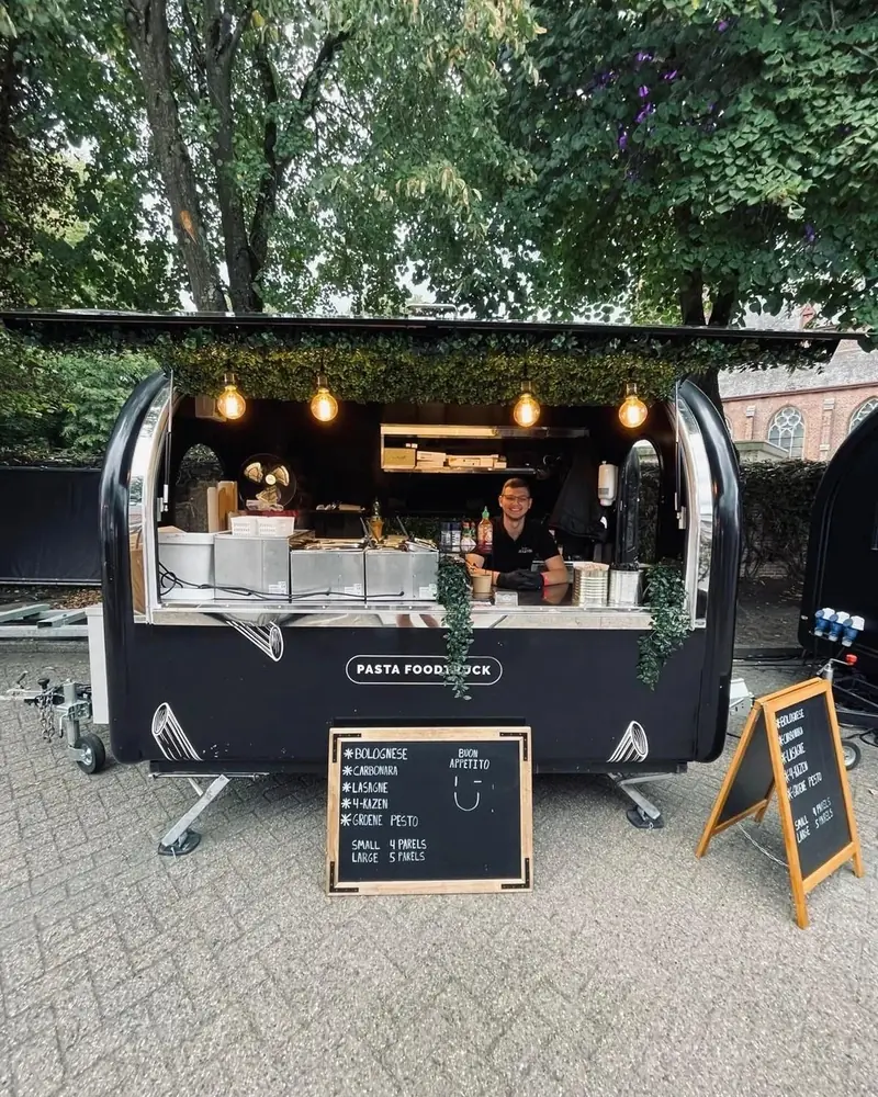 Ronde zwarte foodtrailer van Pasta Deliziosa met lampjes en krijtborden