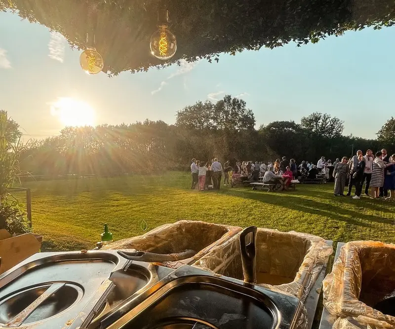 Gasten op een grasveld bij zonsondergang, gezien vanuit de foodtrailer met de sauzen klaar